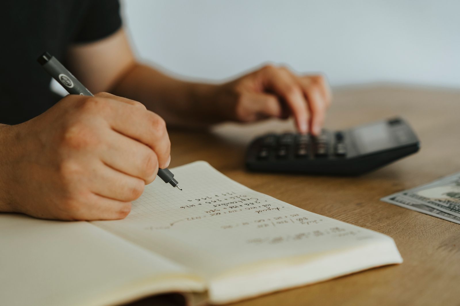 Manos escribiendo cálculos en una libreta con calculadora